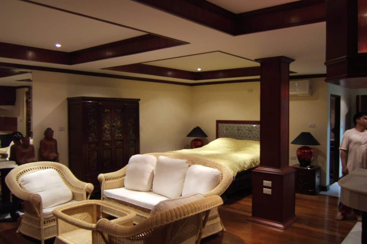 A hotel room with a large bed, two wicker chairs, a wooden cabinet, and a nightstand with a lamp.