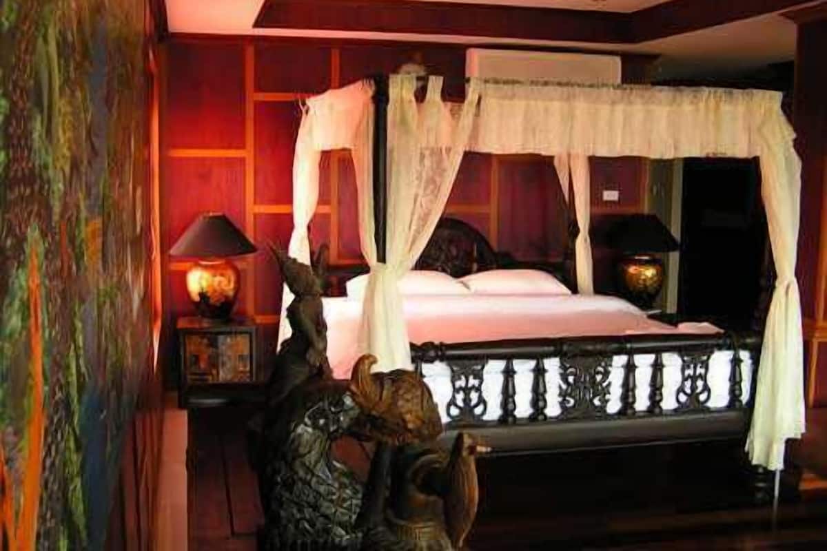 A bedroom with a four-poster bed, a nightstand with a lamp, and a decorative sculpture.