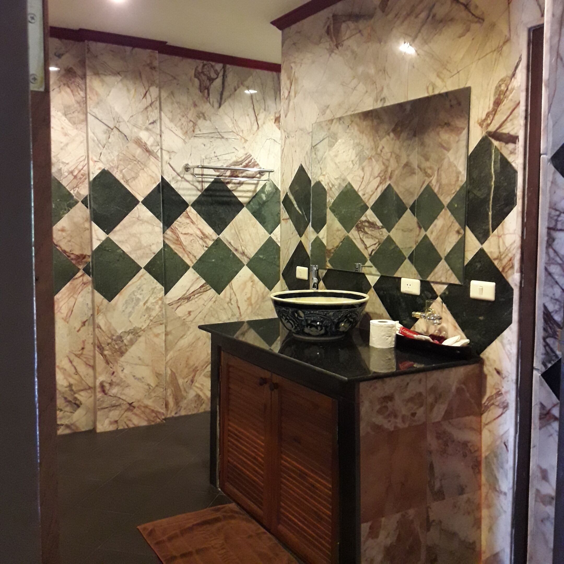 Une salle de bain avec un pare-baignoire en marbre, un lavabo doté d’une cuve noire et un meuble en bois.