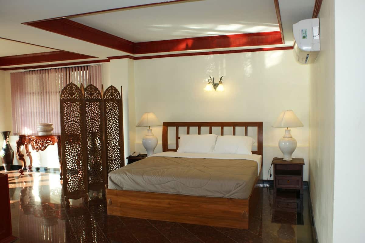 A hotel room with a wooden bed, two bedside lamps, a decorative screen, and a wall-mounted air conditioner.