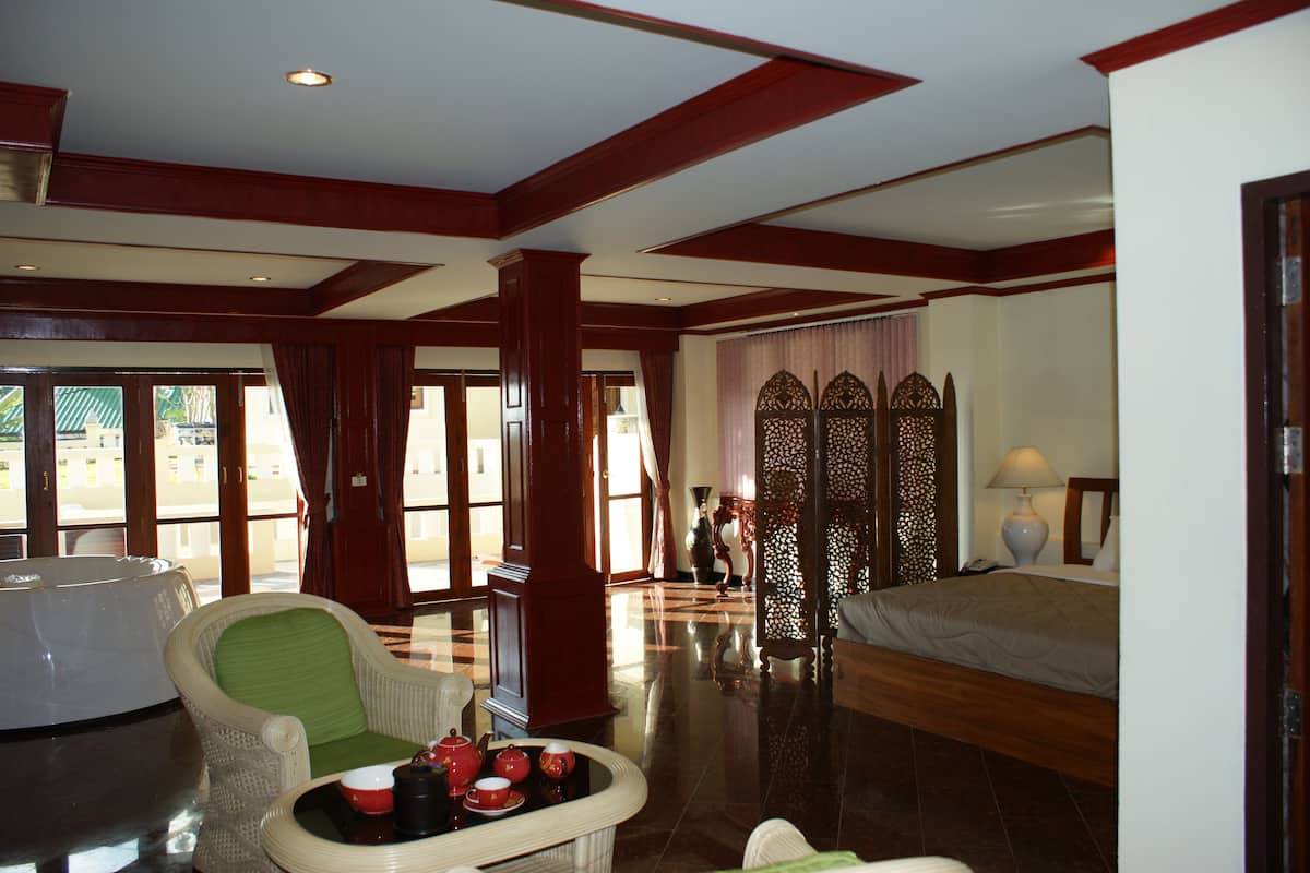 A hotel room with a bed, a chair, a table with teapots, and a decorative screen.