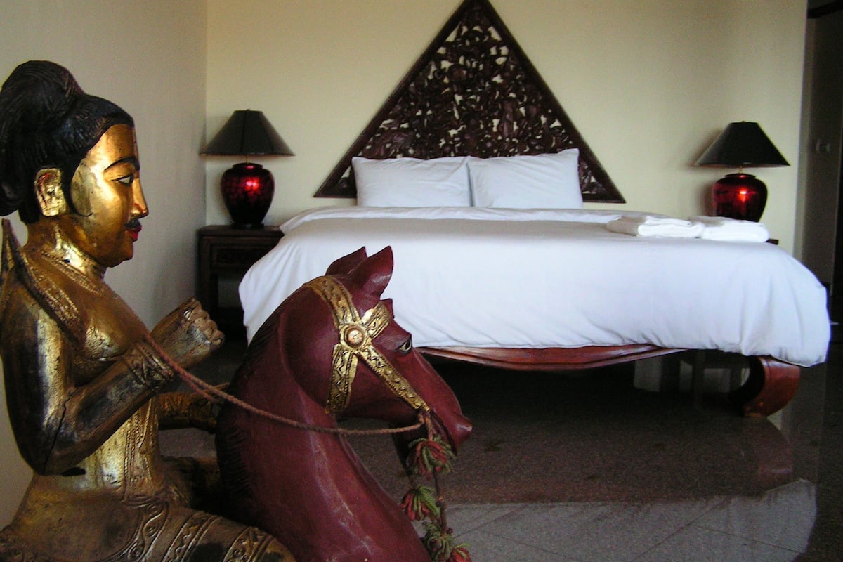 A room with a bed, two lamps, a statue, and a decorative wall panel.