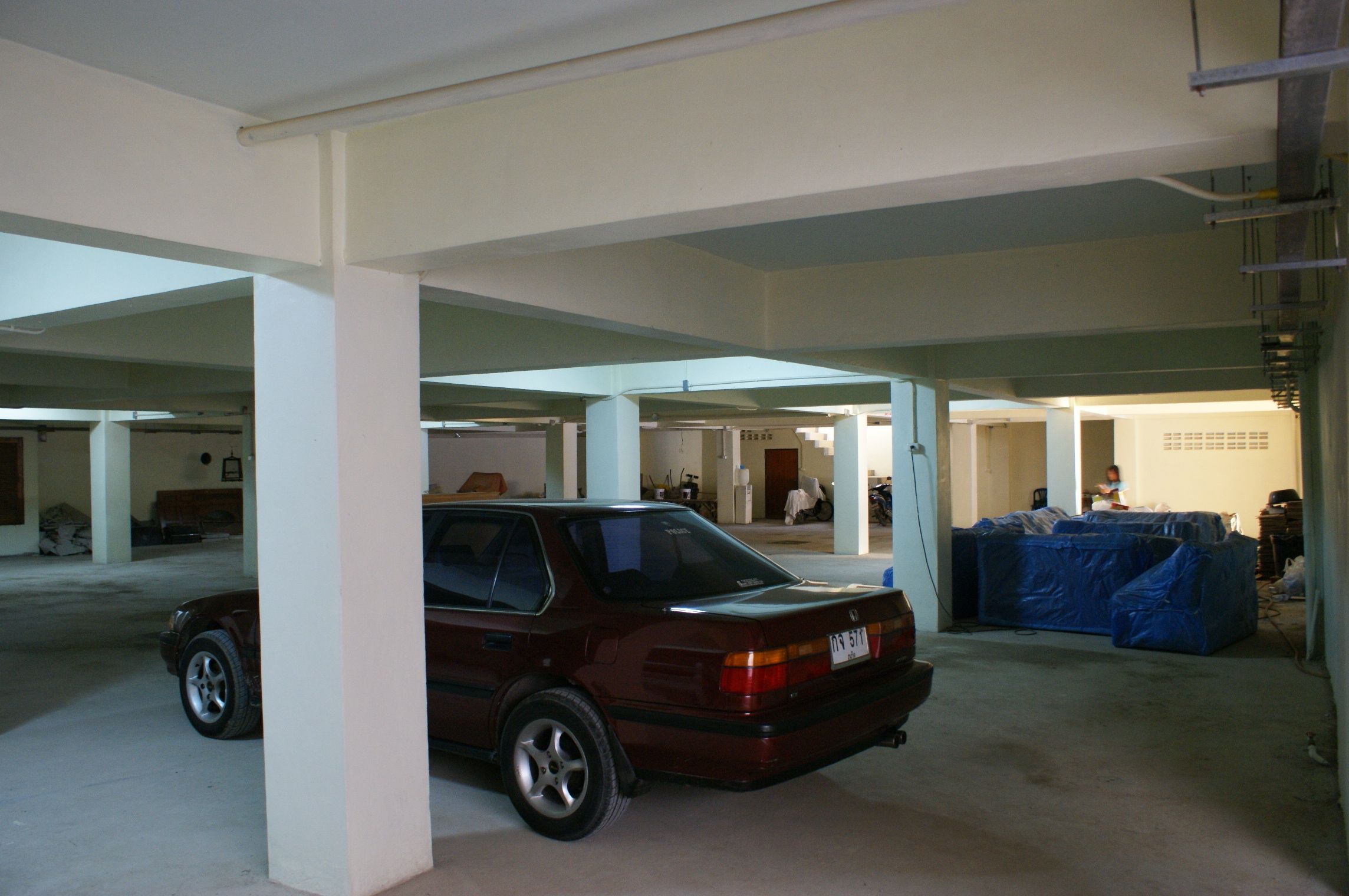Un parcheggio con un'auto color borgogna parcheggiata vicino a un oggetto azzurro coperto.