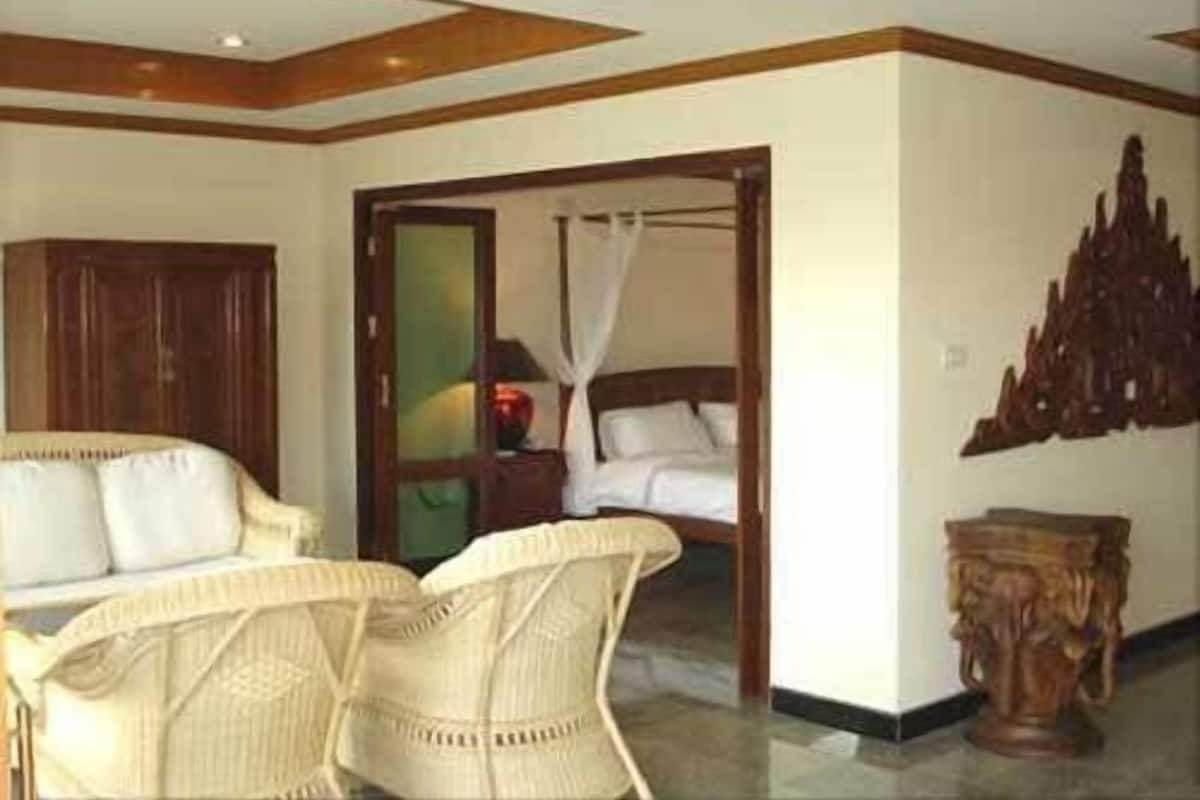 A hotel room with a bed, a sitting area with chairs, a wooden cabinet, and a decorative wall piece.