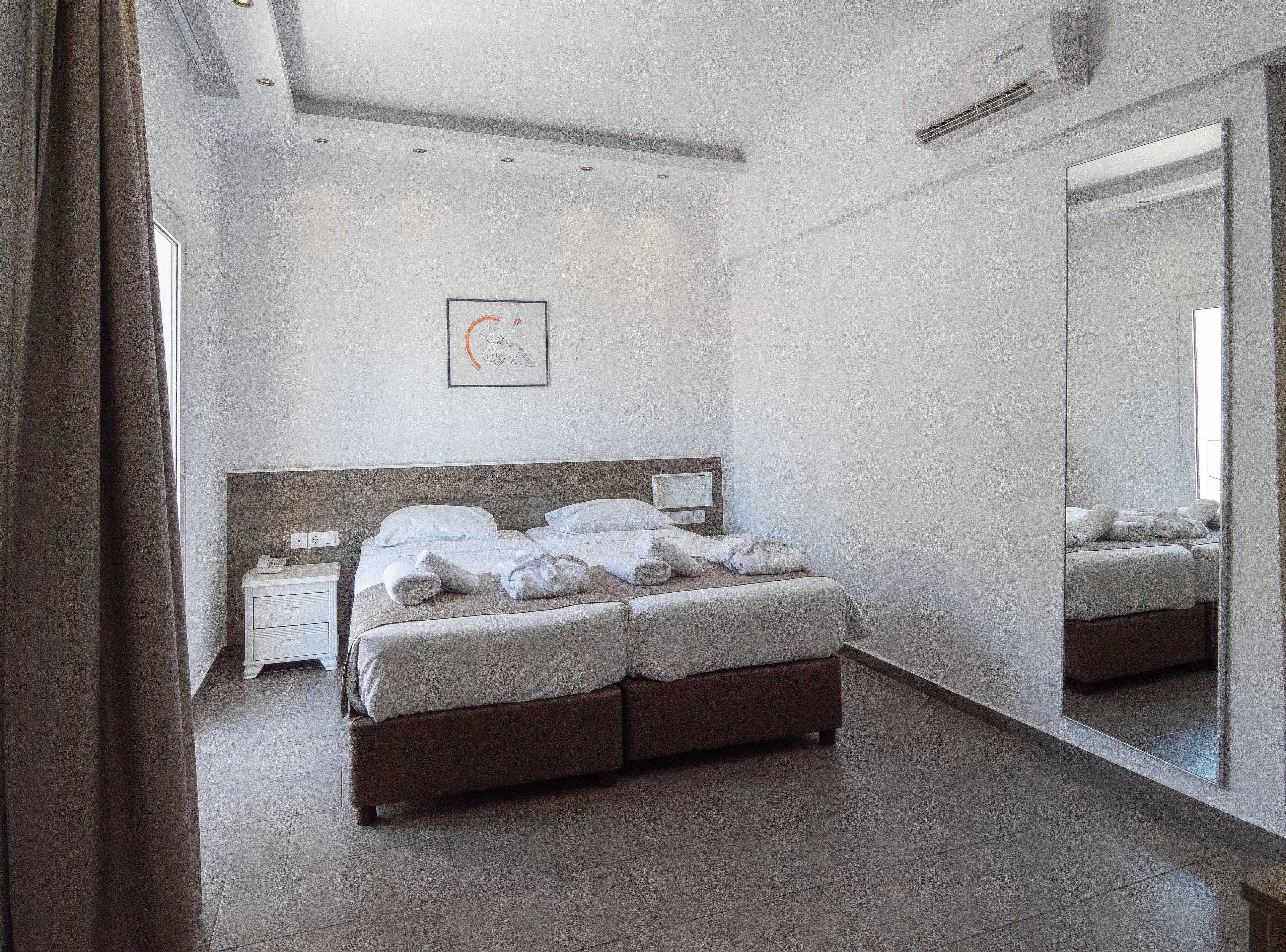A modern hotel room with a large bed, bedside tables, a mirror, and a ceiling light.