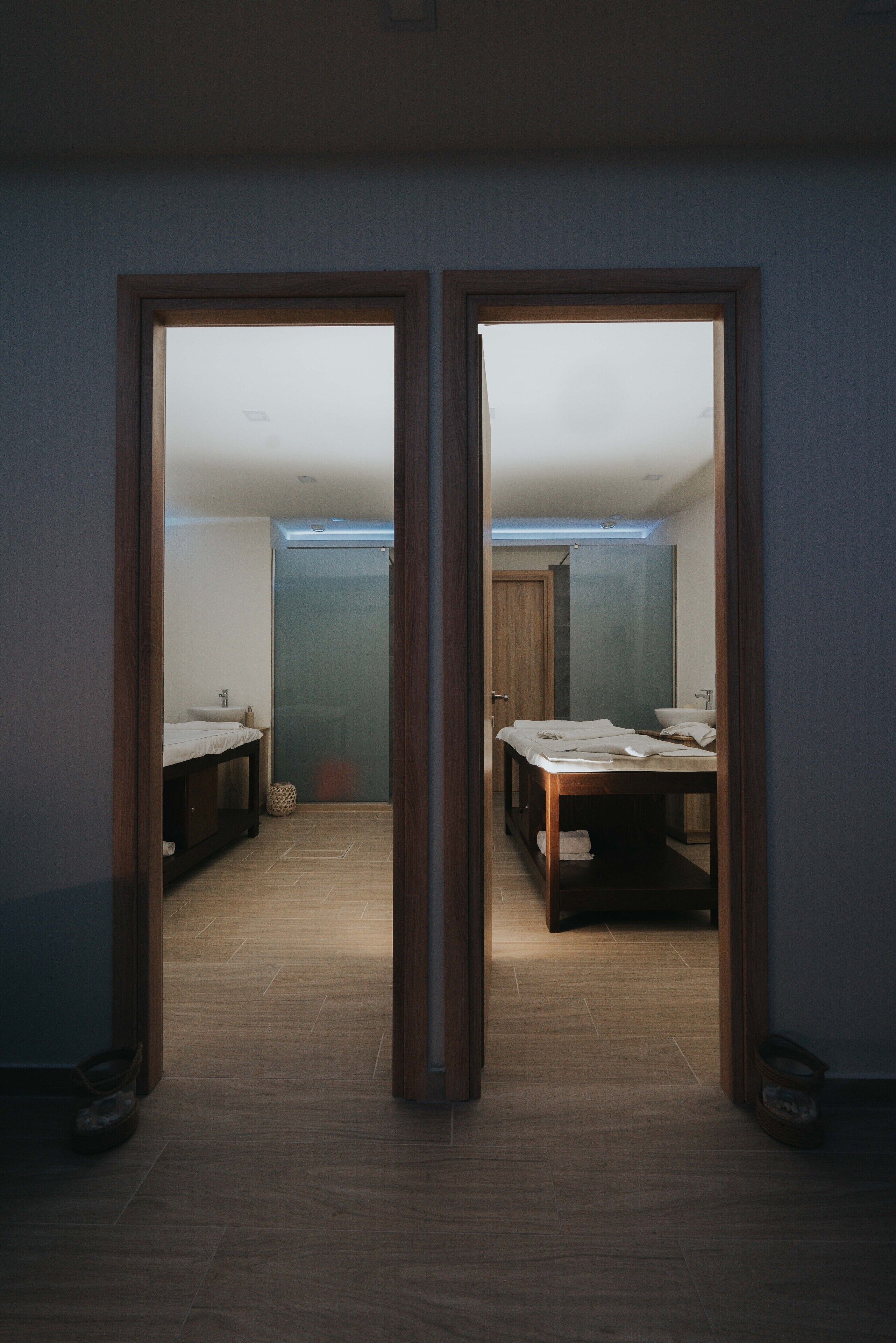 A room with a bed, a small table, and a mirror. There is a door leading to another room.