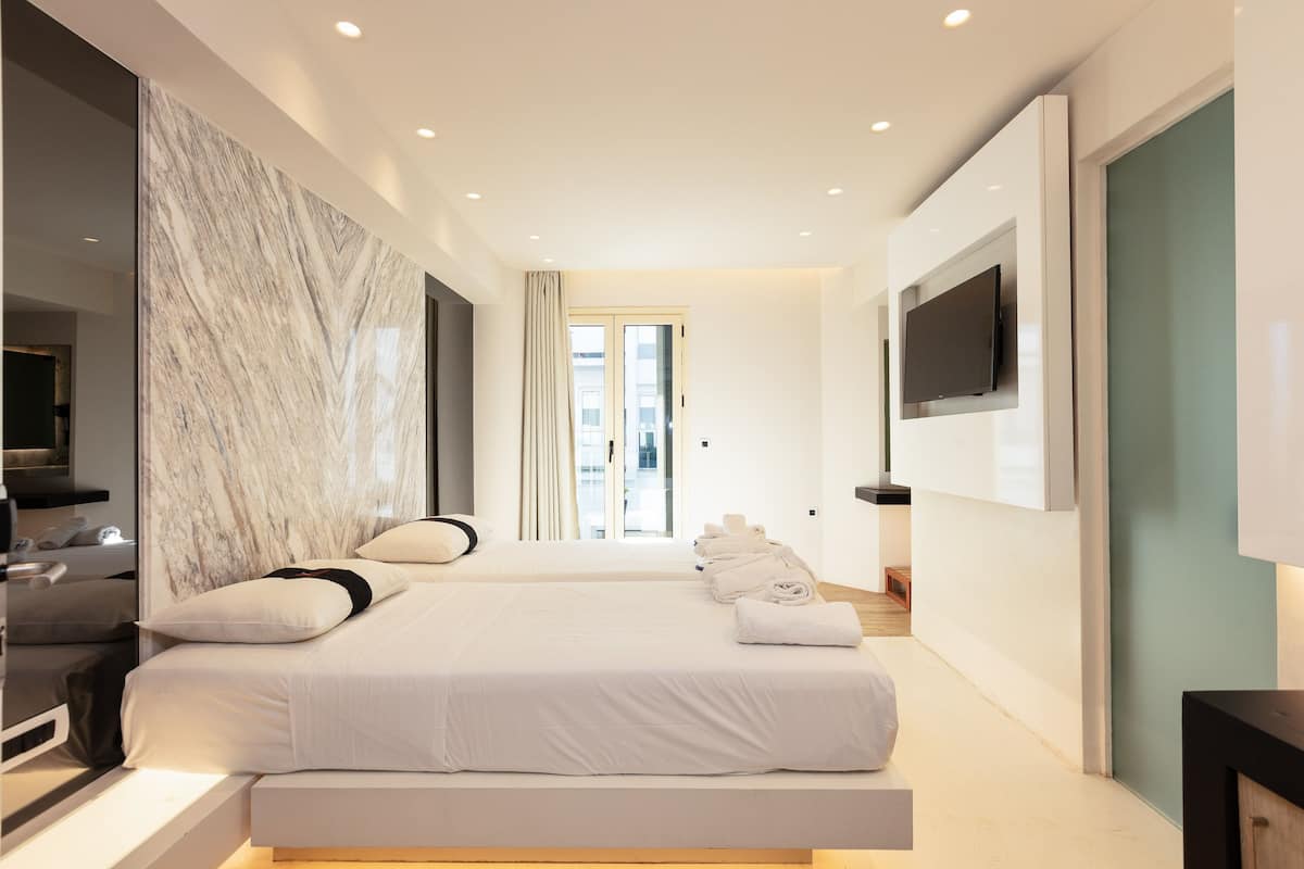 A modern hotel room with a large bed, a flat-screen TV mounted on the wall, and a marble accent wall.
