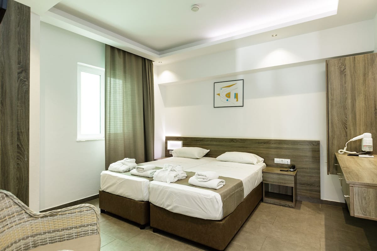 A hotel room with two beds, a bedside table, a chair, a desk, and a mirror.