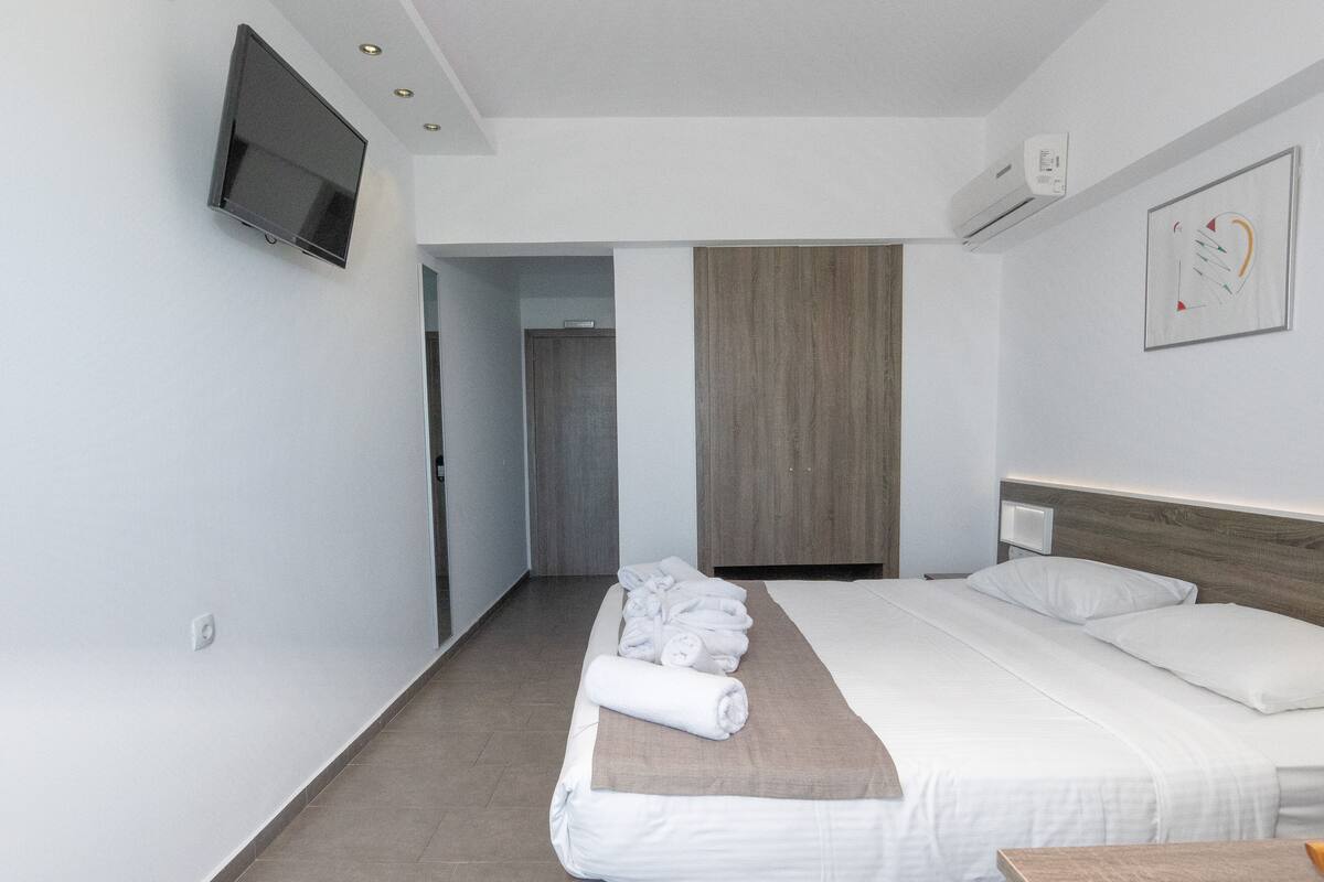 A hotel room with a bed, a TV mounted on the wall, and a wooden headboard.