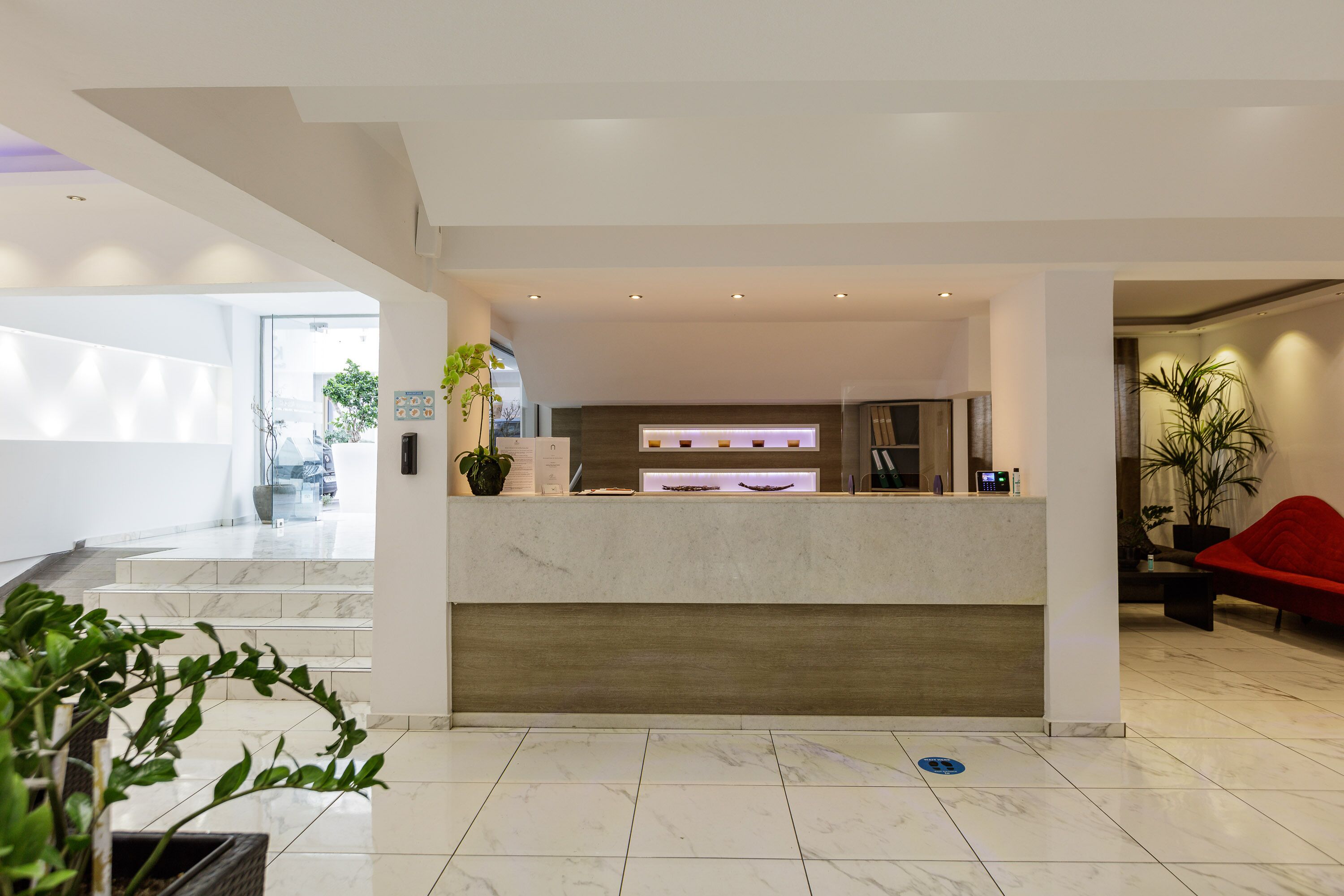 A modern hotel lobby with a reception desk, marble flooring, and potted plants.