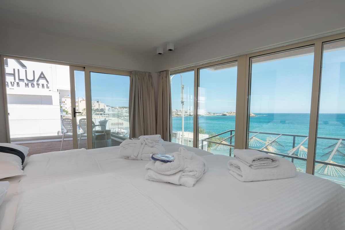 A hotel room with a large bed, two towels, and a view of the sea.