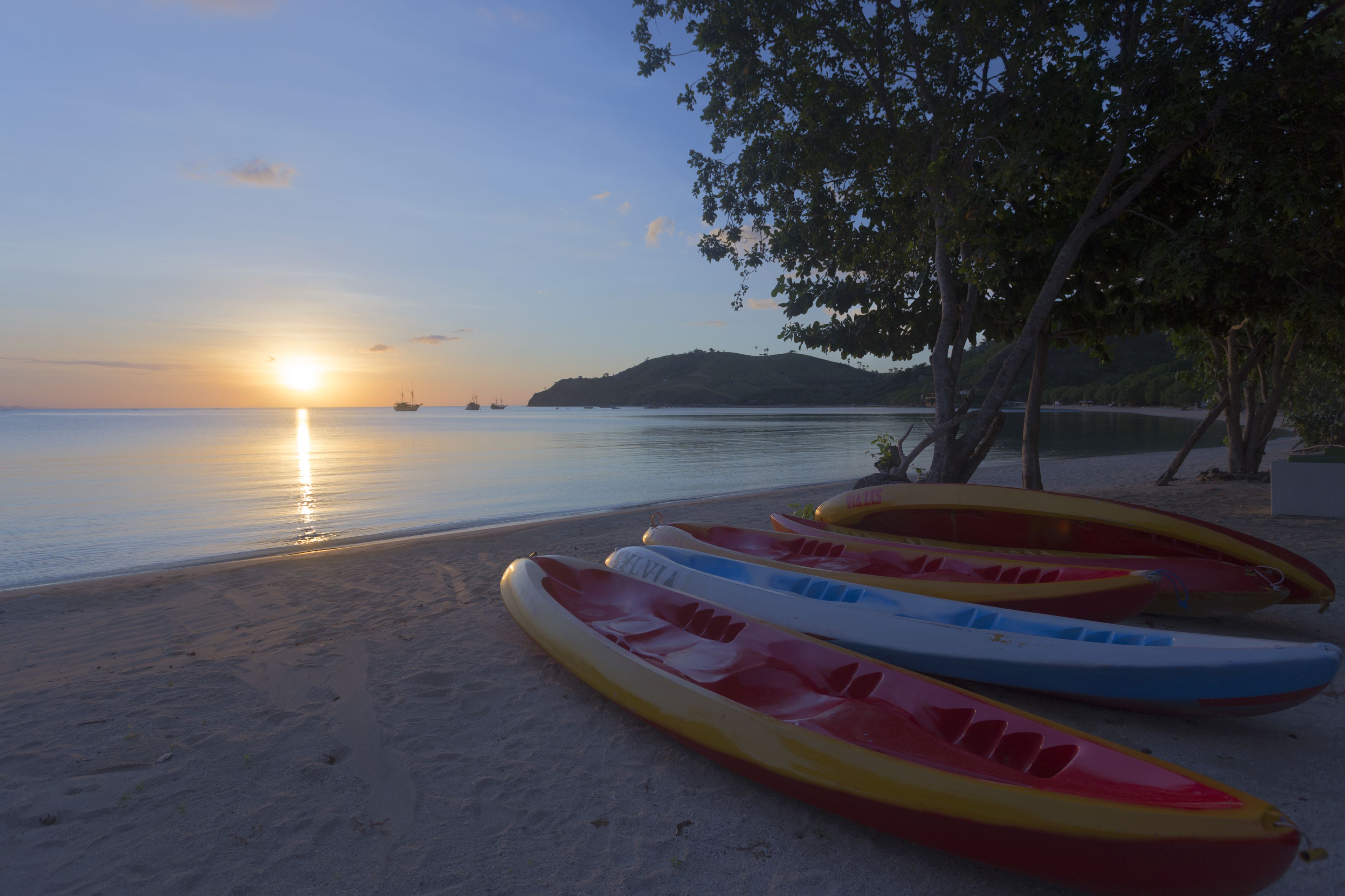 A beach with kayaks lined up and a sunset in the background.