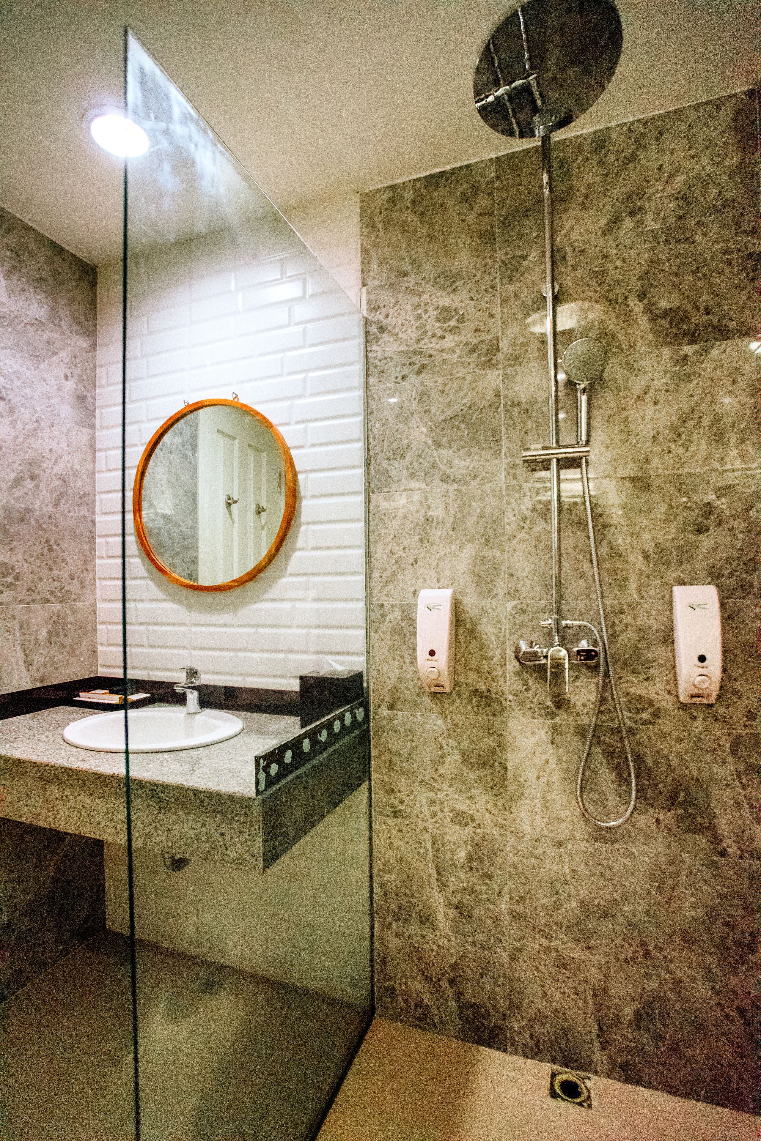 Un baño moderno con separador de vidrio, espejo redondo, lavabo y ducha.