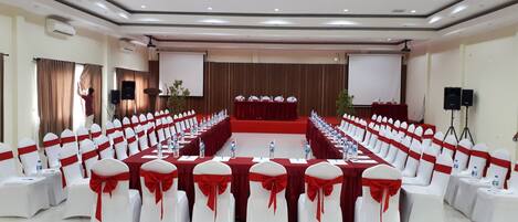 A conference room with a long table, white chairs with red sashes, a podium, and a projector screen.
