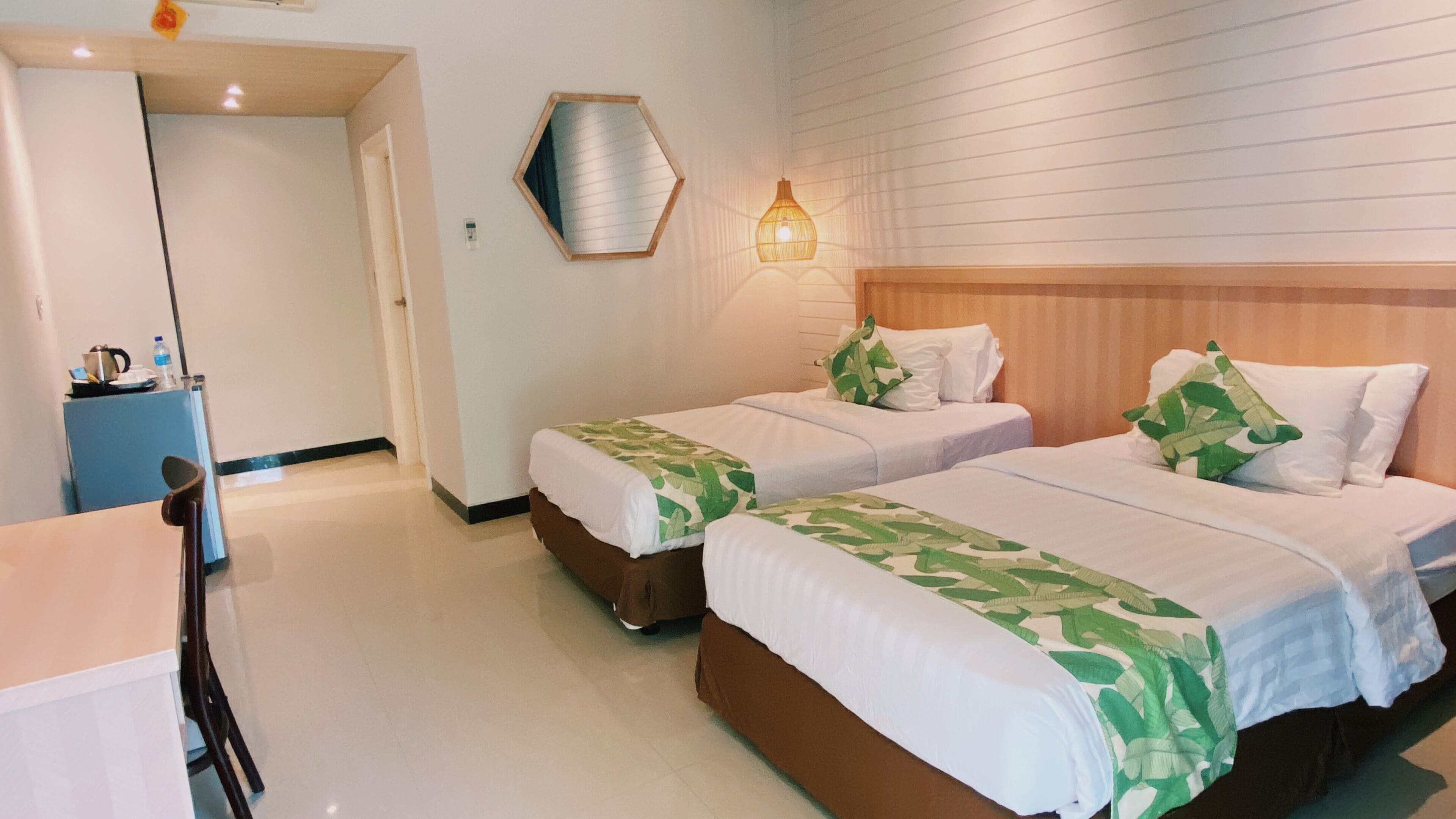 Ein Hotelzimmer mit zwei Betten, einem Holzkopfstück, einer Wandleuchte und einem kleinen Schreibtisch mit Stuhl.