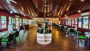 Ein großzügiges Restaurant mit hohen Decken, mehreren Deckenventilatoren und großen Fenstern, die den Blick ins Grüne gewähren.