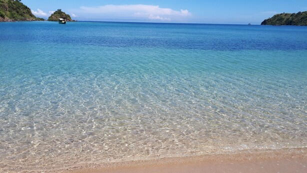 Ein sauberer Strand mit ruhigem Wasser und sanften Hügeln im Hintergrund.