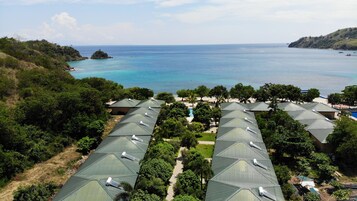 Un resort con varias construcciones con techos verdes, una piscina y vista al océano.