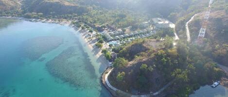 An aerial view of a coastal resort with a marina, clear turquoise waters, and lush greenery.