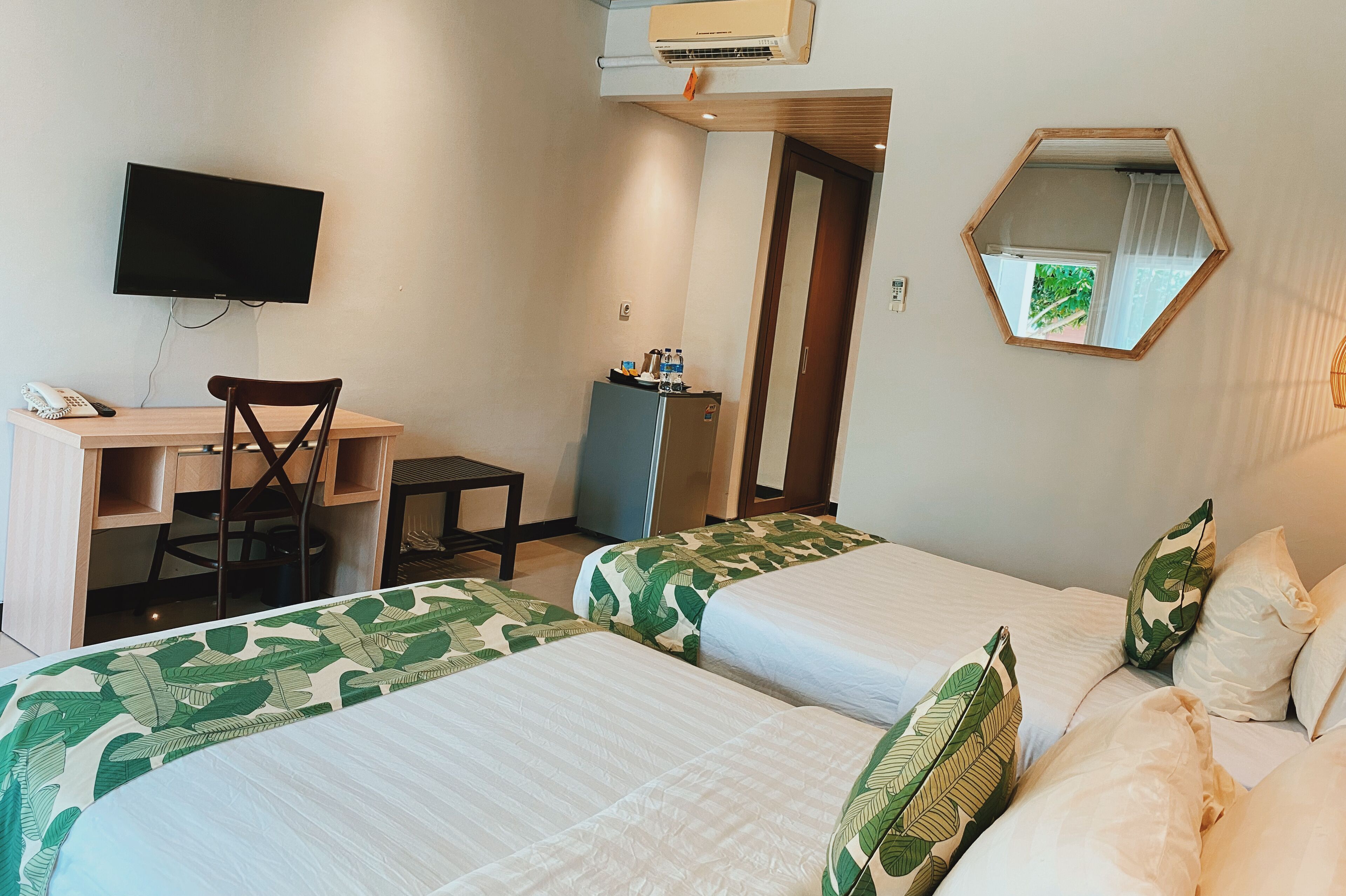 A hotel room with two beds, a desk, a chair, a television, a mirror, and a small refrigerator.