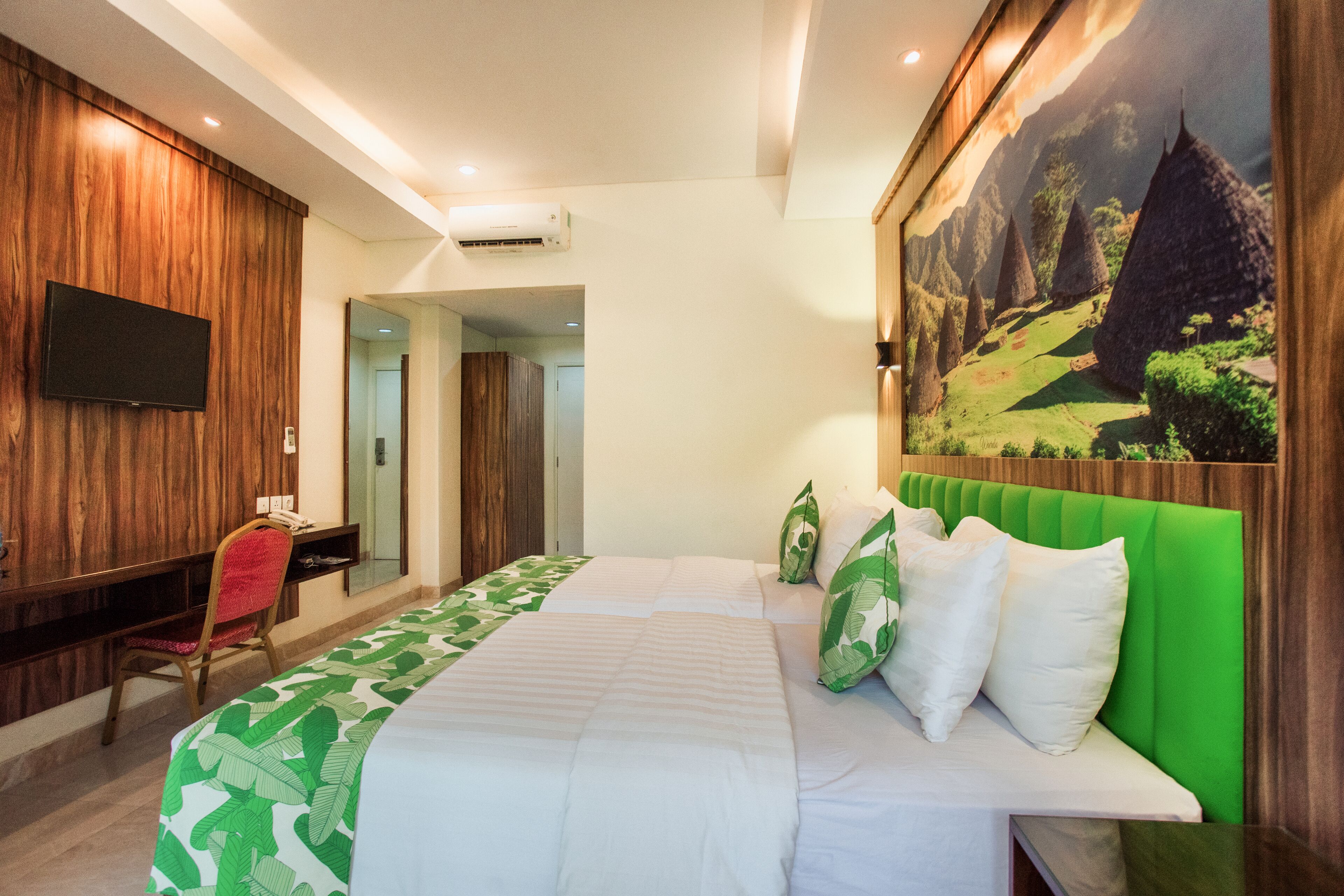 Habitación de hotel con cama, escritorio, televisión y un cuadro de un paisaje montañoso.