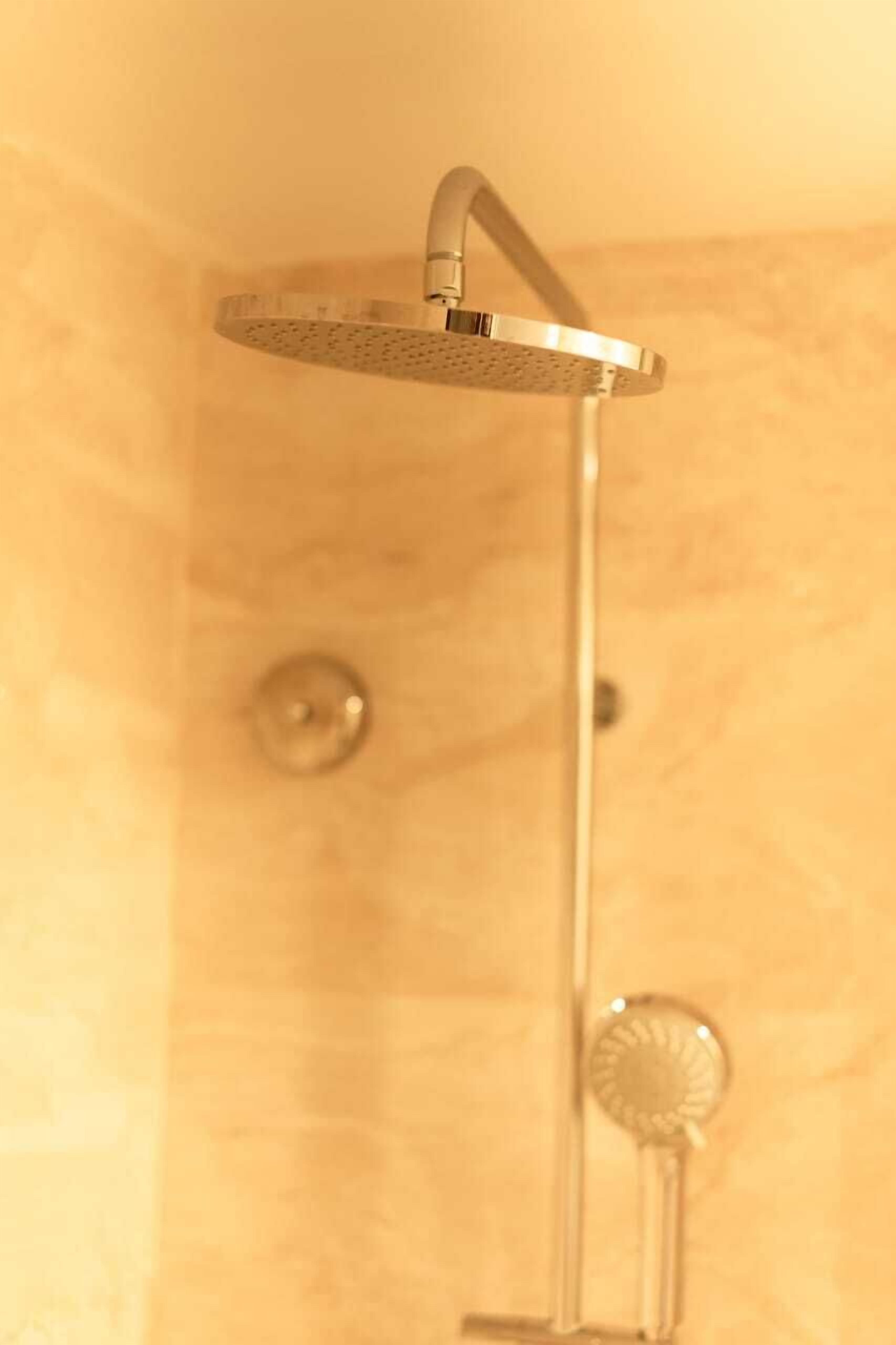 Ein Duschkopf mit kreisförmigem Sprühbild, ein an der Wand befestigtes Bedienknopf und ein sichtbarer Abfluss.