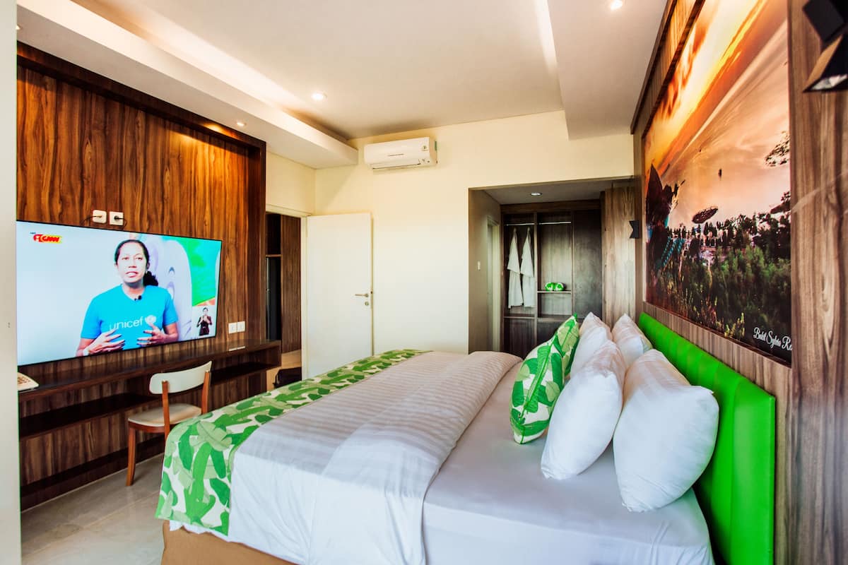 Ein Hotelzimmer mit einem Bett, einem Fernseher, einer Holzwand und einem grünen Kopfteil.