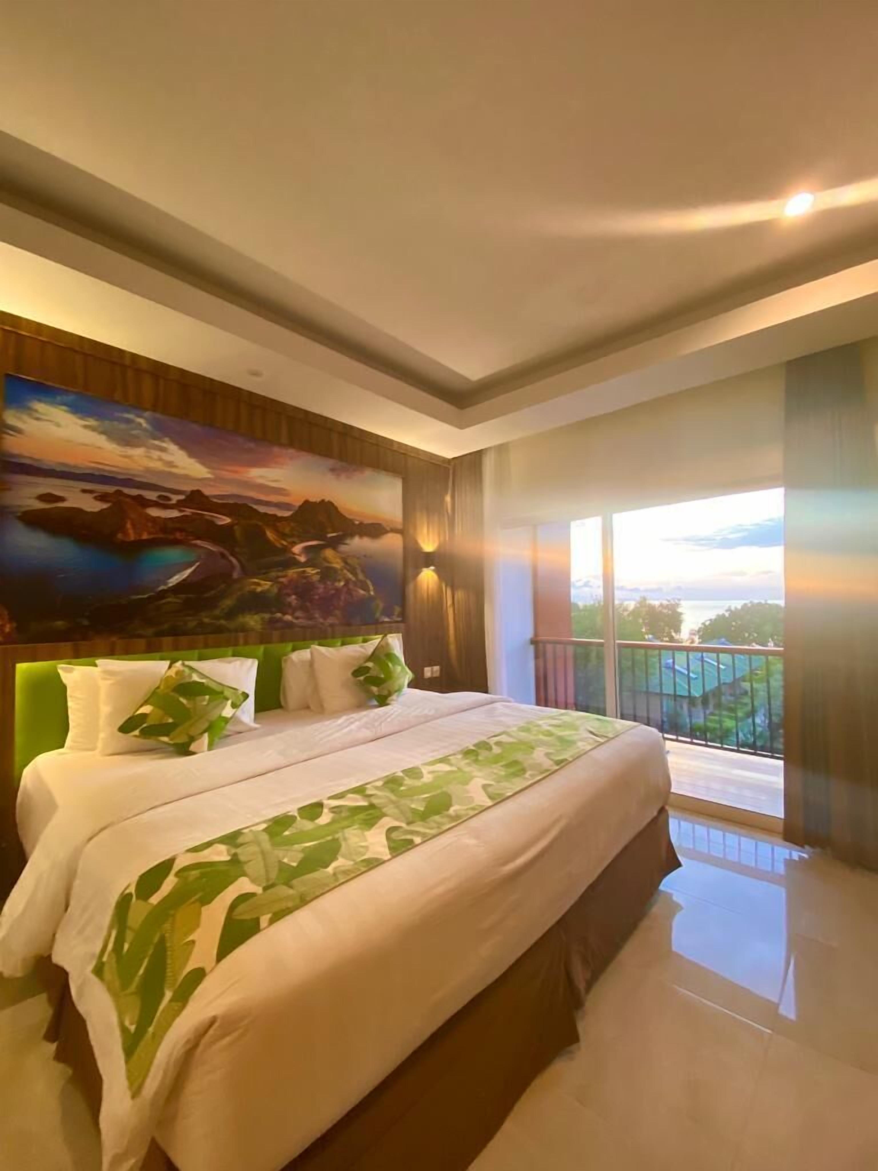 A hotel room with a large bed, a painting on the wall, and a balcony with a view.