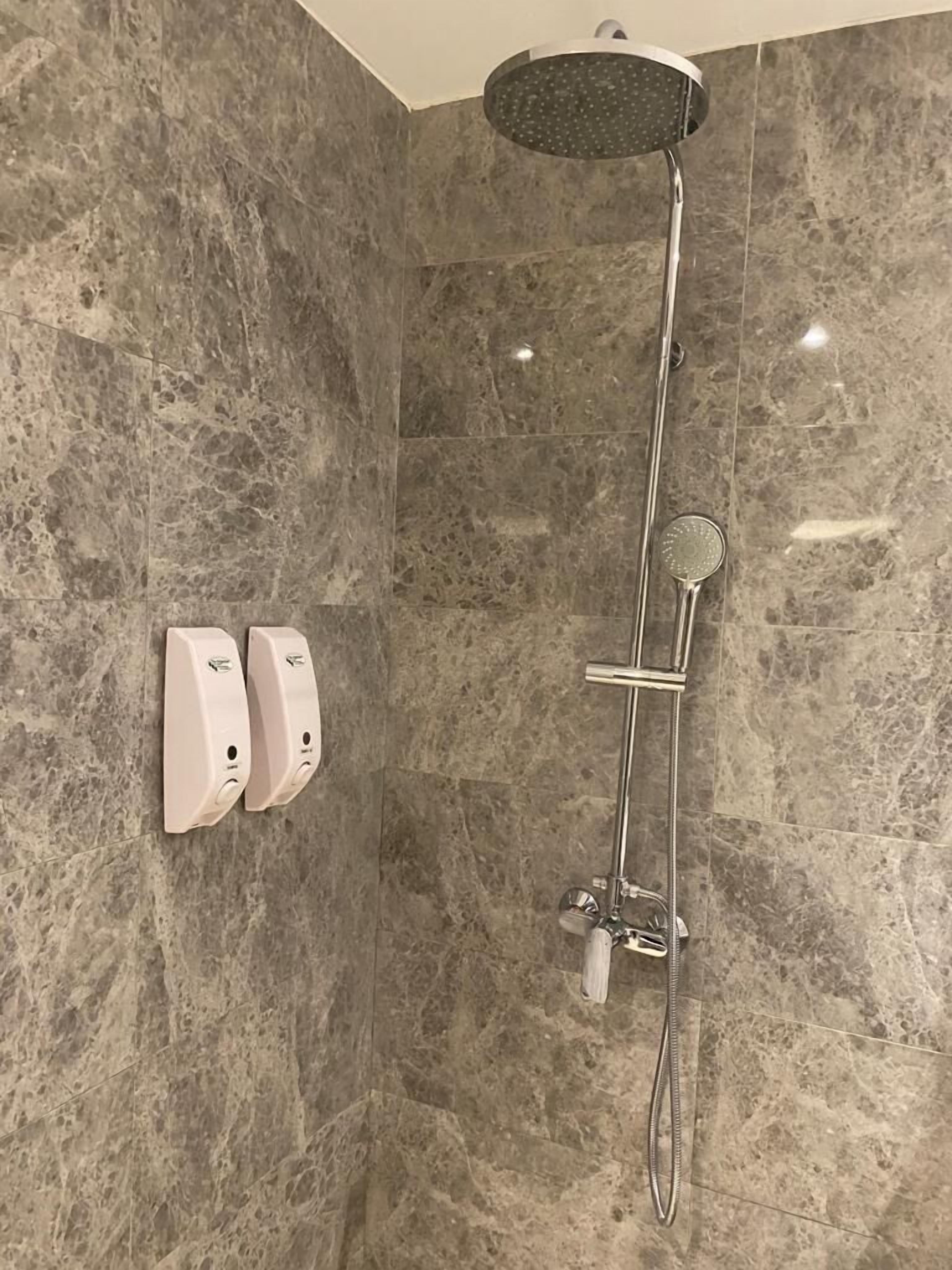 A modern shower with a rain showerhead and handheld showerhead, mounted on a marble wall.