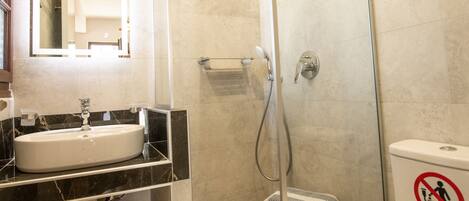 Un baño moderno con ducha de vidrio, un lavabo blanco y un inodoro.