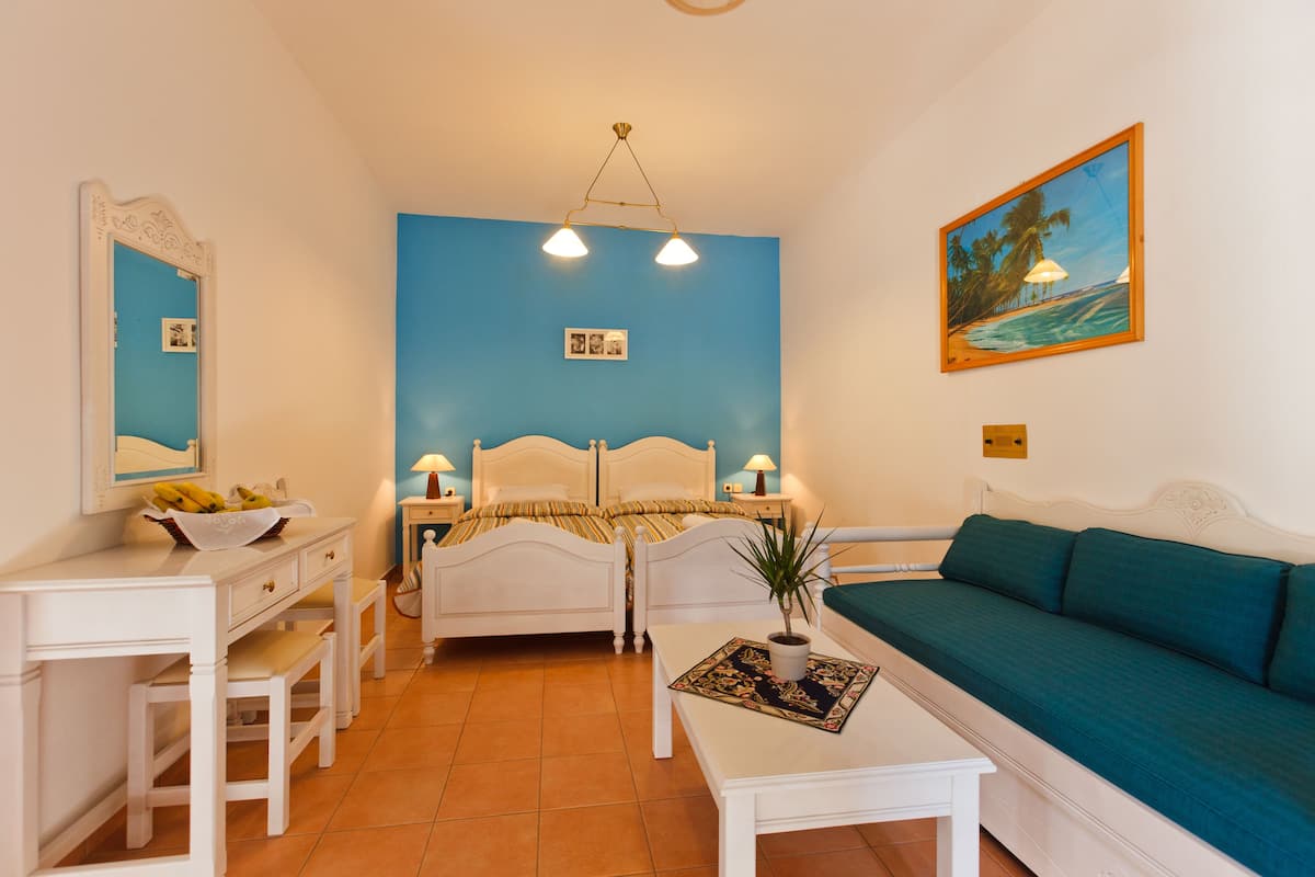 Une chambre à coucher comprenant un lit, un bureau, une chaise, un canapé, une table de chevet, une lampe, un tableau accroché au mur et une plante en pot.
