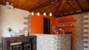 A bar area with a stone counter, wicker stools, and a variety of bottles on shelves. - Hovolo Hotel Apartments (Skopelos)