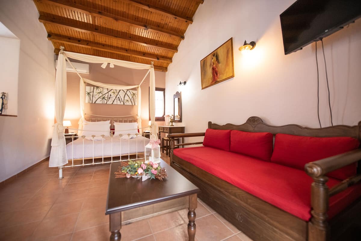 Une chambre à coucher avec un lit à baldaquin, un canapé rouge, une table basse en bois et un téléviseur fixé au mur.