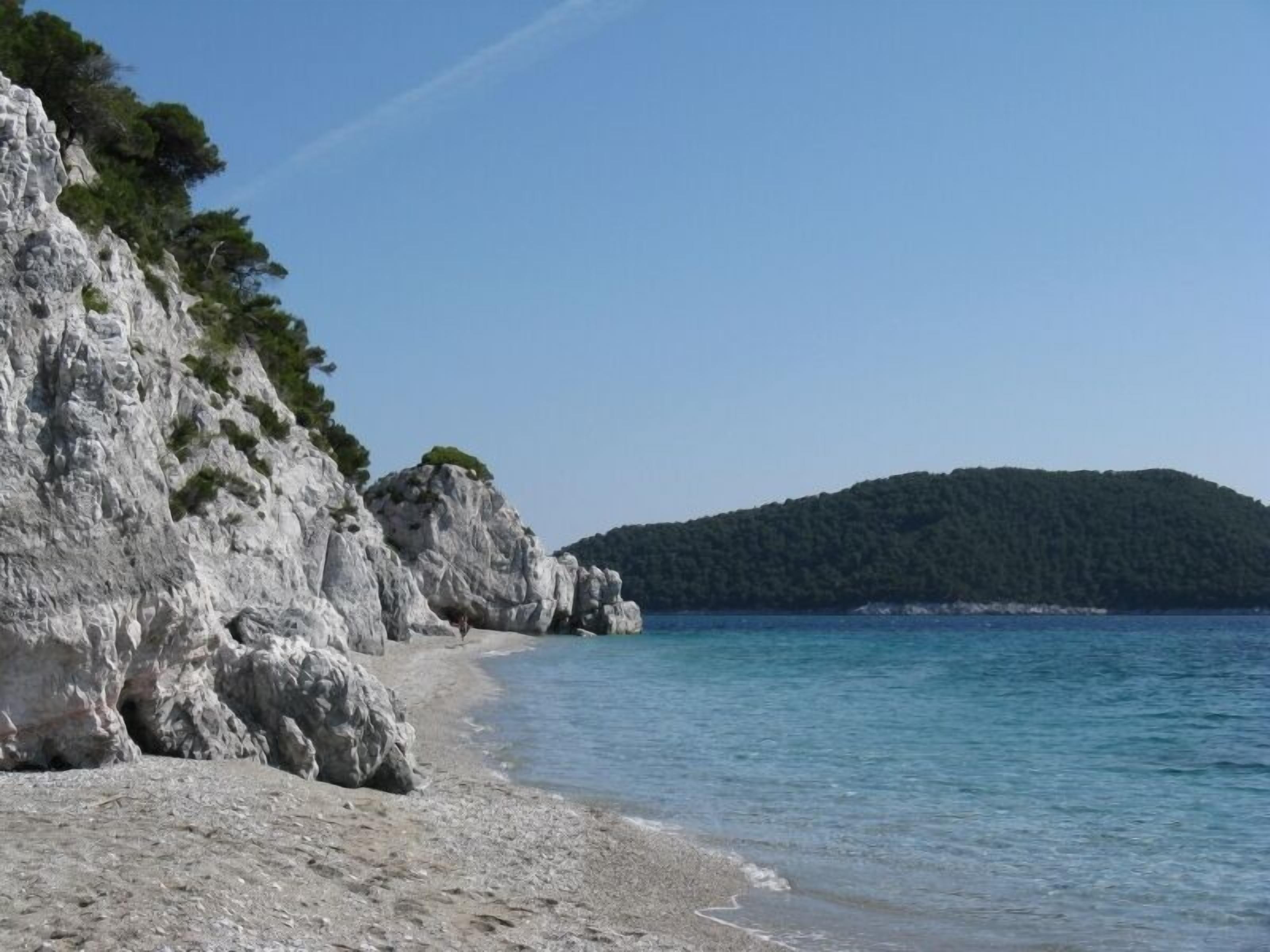 A coastal beach with rocky cliffs and a clear blue sea.