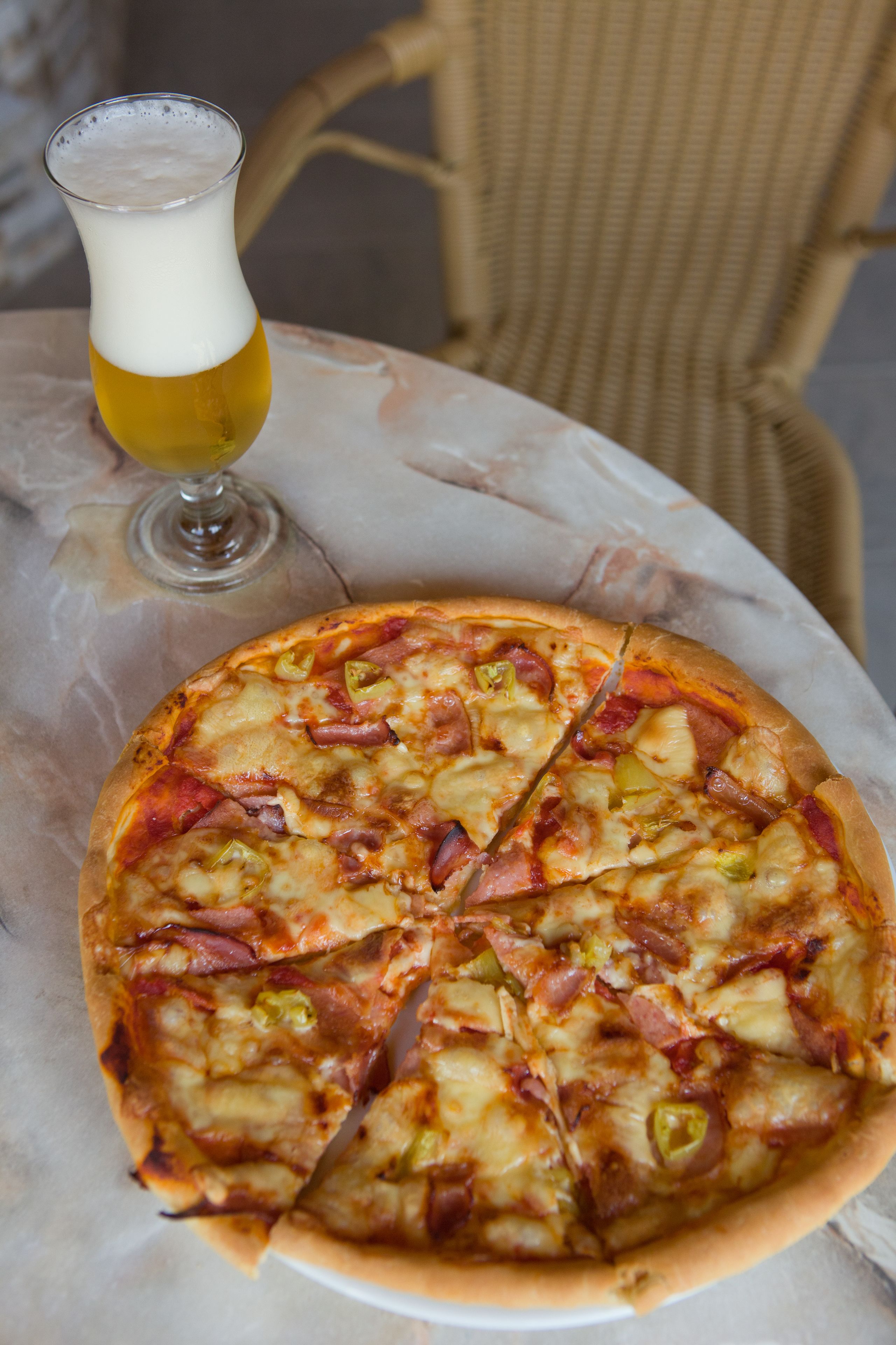 Eine Pizza auf einem runden Tisch, daneben ein Glas Bier.