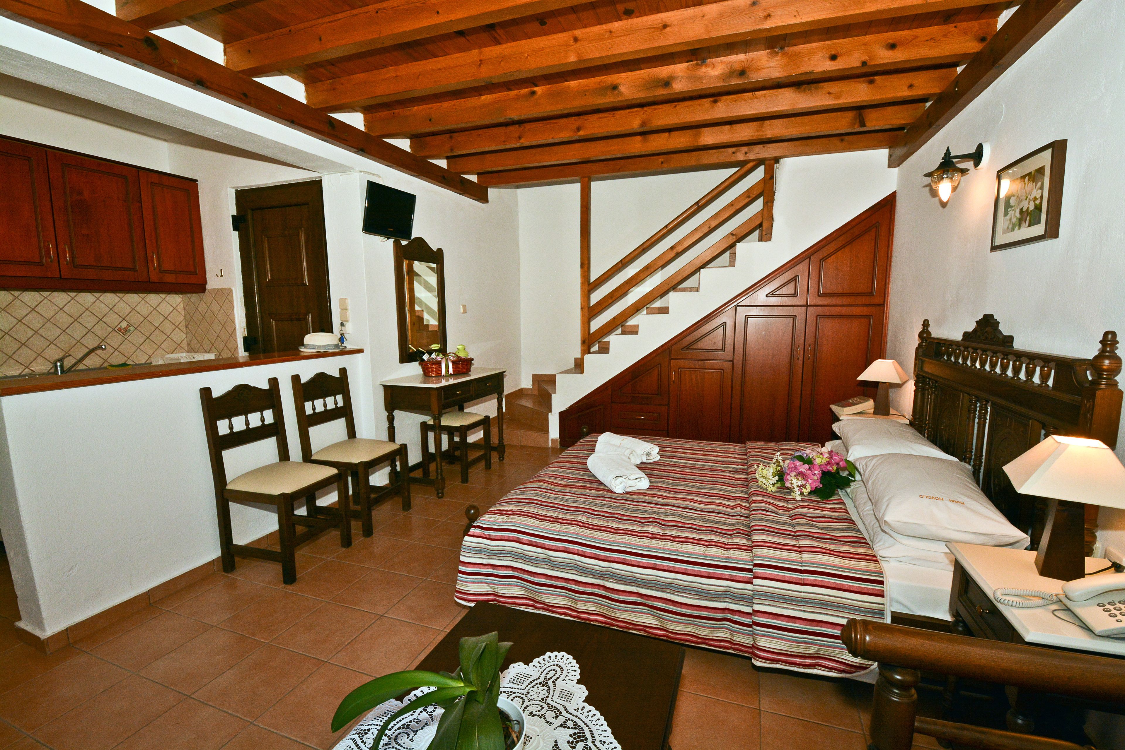 Ein Schlafzimmer mit einem hölzernen Bett, einem Schreibtisch mit Stühlen, einer Treppe und einer kleinen Küchenzeile.