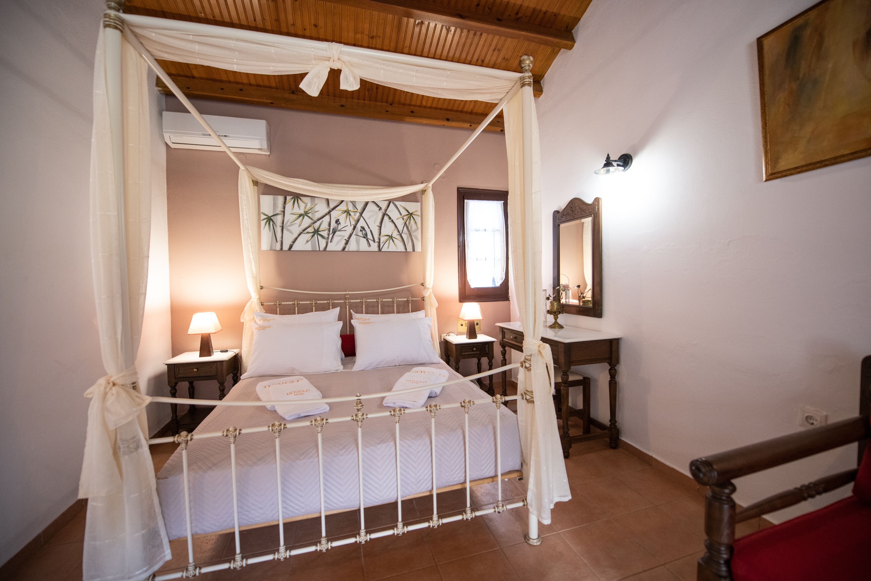 A four-poster canopy bed with white linens and a wooden headboard. There are two bedside tables with lamps and a small mirror.