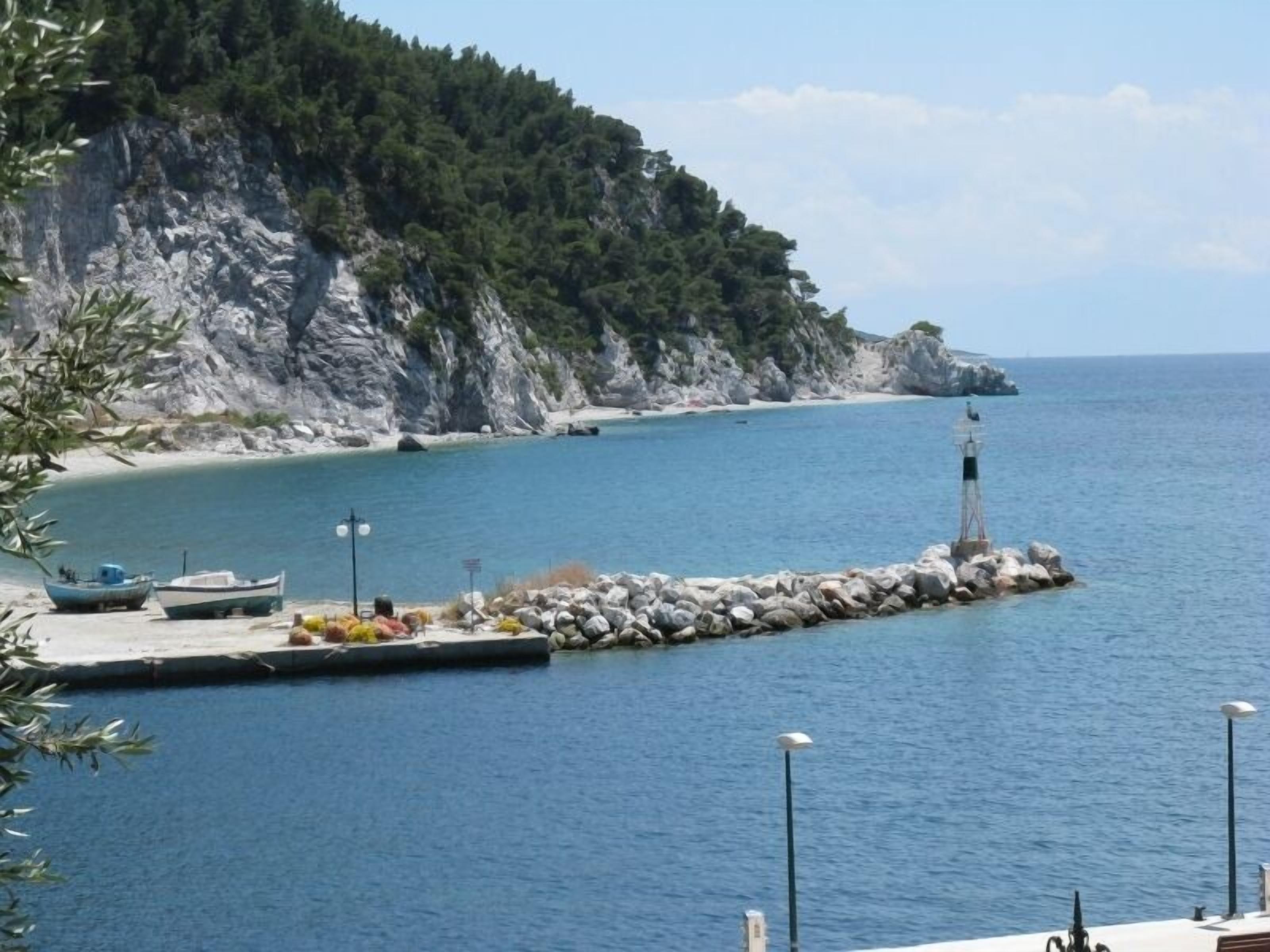 A coastal scene with a rocky pier, boats, and a lighthouse.