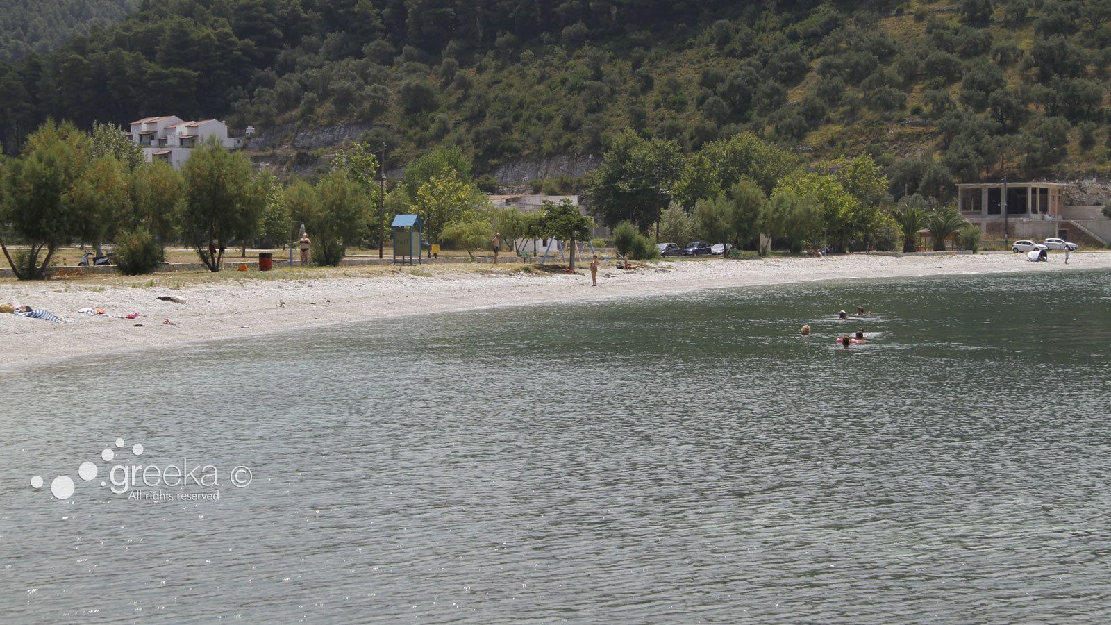 A beach with a row of buildings in the background, a clear view of the water, and a few people swimming.