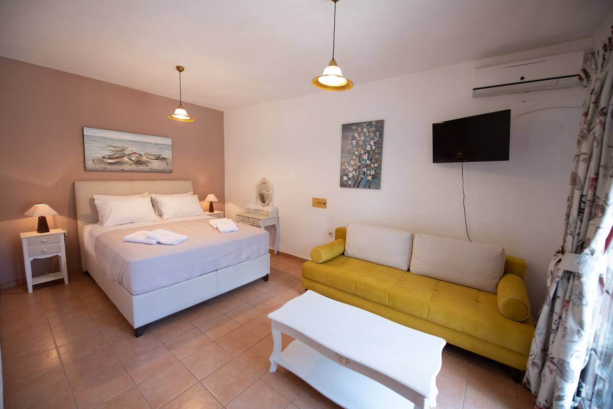 Une chambre à coucher comprenant un lit, des tables de chevet, un canapé, un téléviseur et des œuvres d’art accrochées aux murs.
