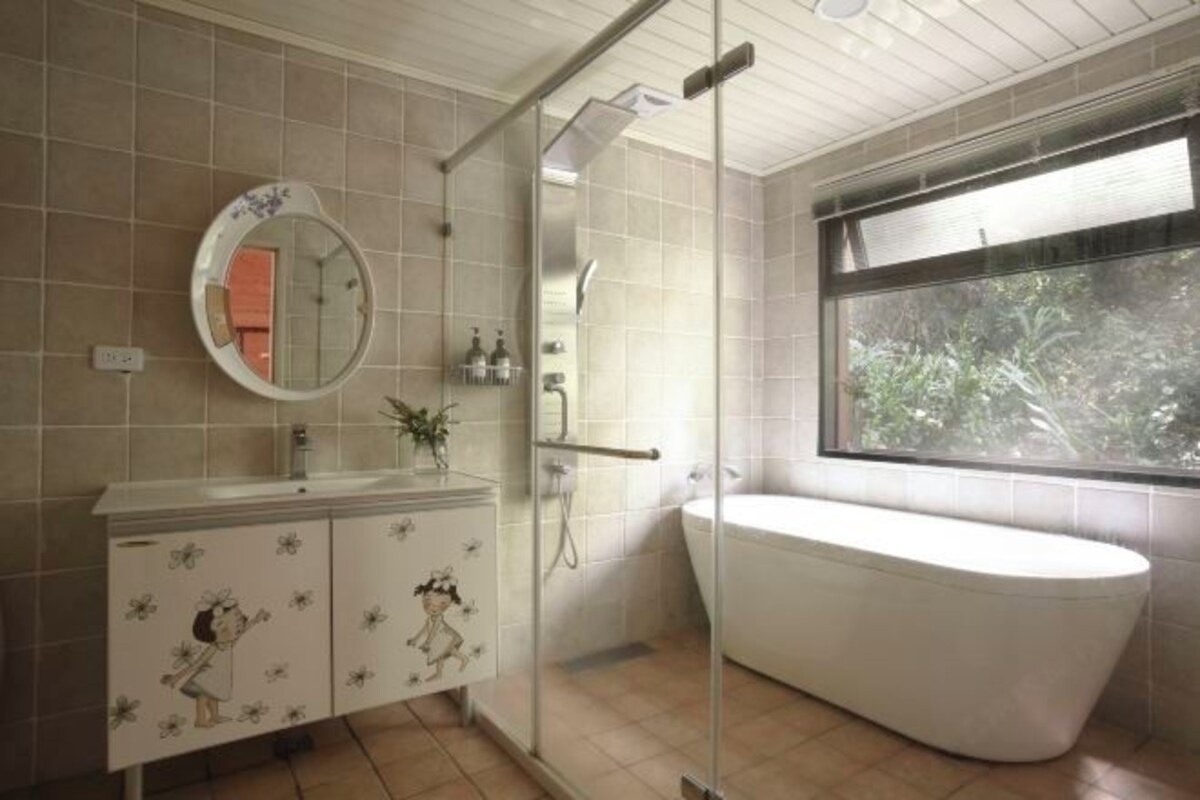 Un baño con cabina de ducha de vidrio, una bañera blanca, un espejo redondo y un mueble con diseños florales.