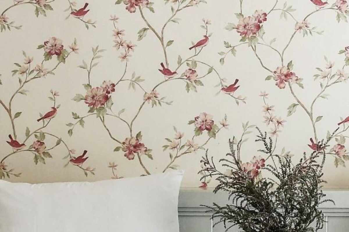 Una habitación con estampado floral en el papel tapiz, un almohadón blanco y una planta en maceta.