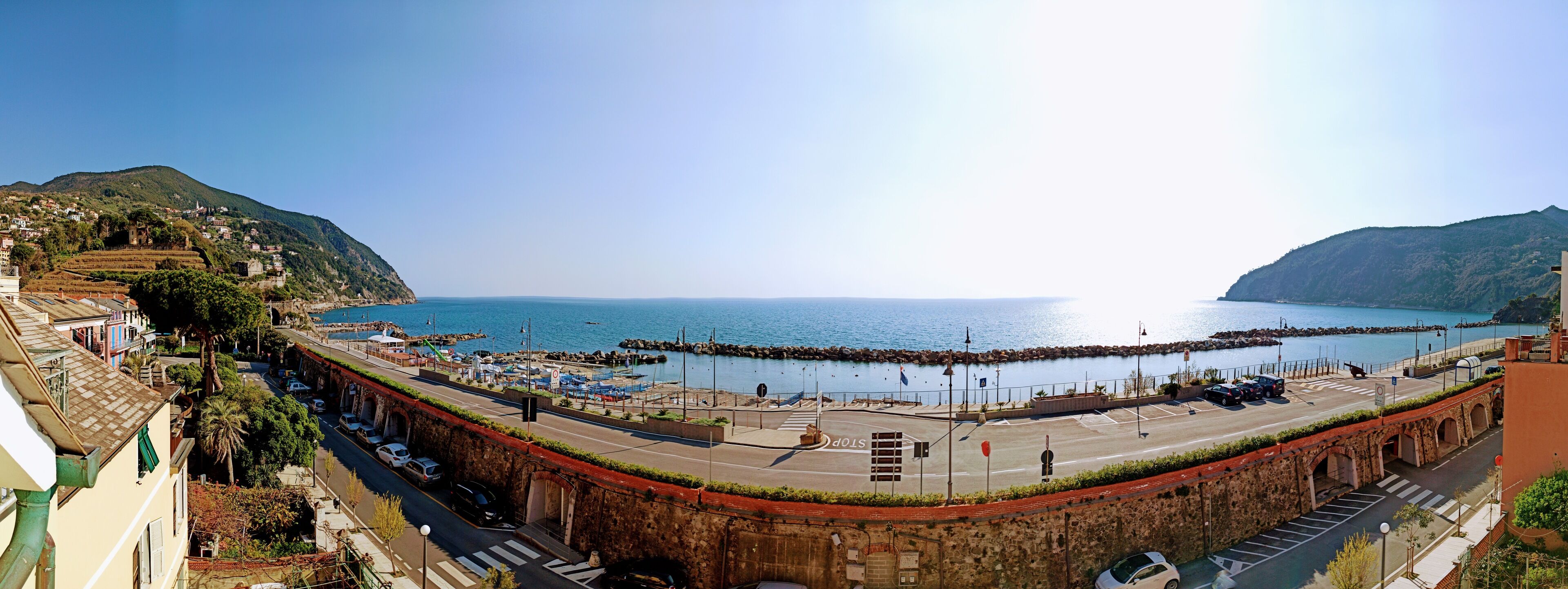 A coastal town with a prominent stone bridge, a marina, and a clear view of the sea.