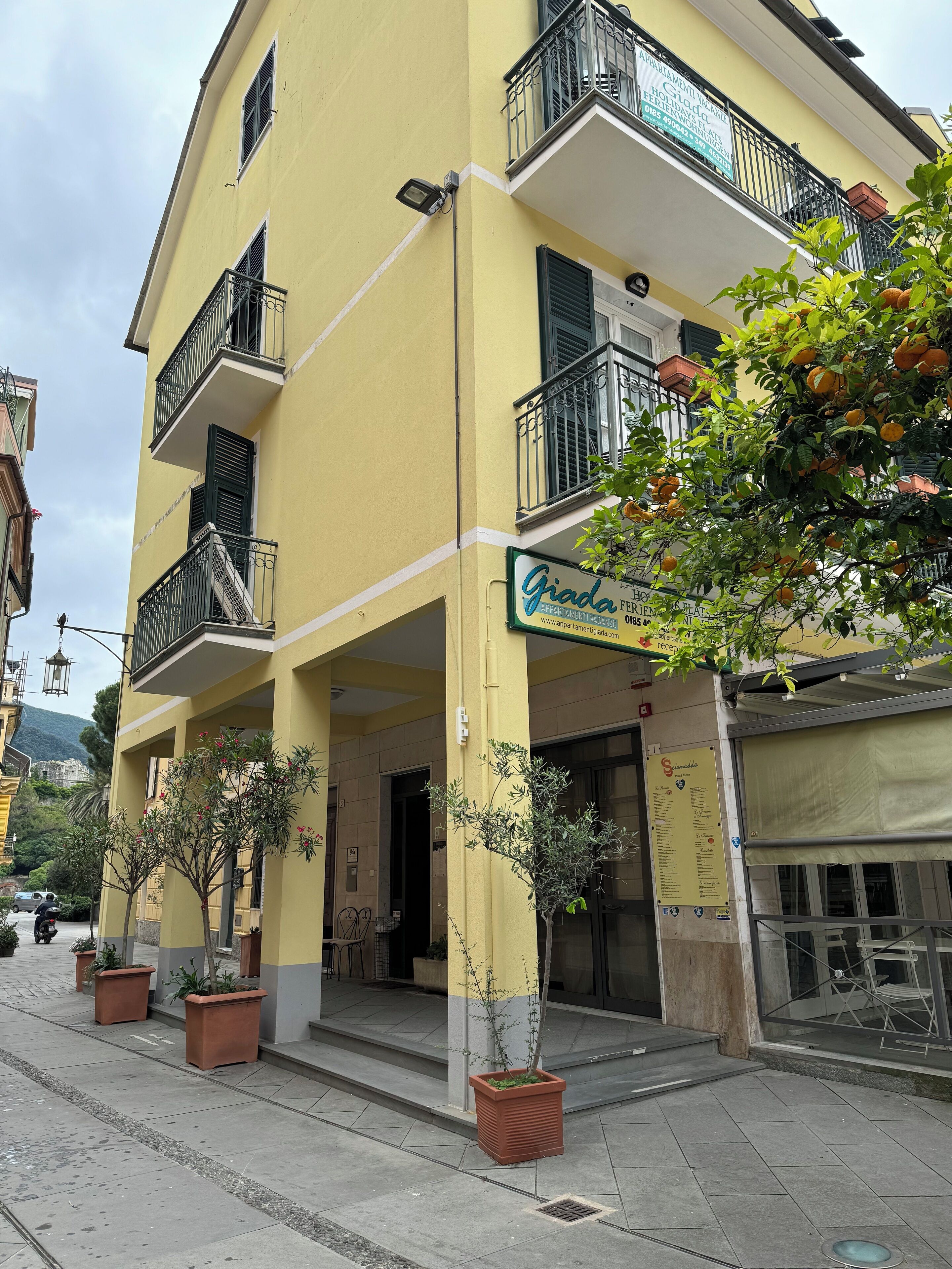 A yellow building with balconies, potted plants, and a sign for 'Giada'.