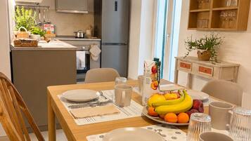 Una cocina moderna con refrigerador, estufa y armarios. Hay una mesa de comedor con platos, cubiertos y un frutero.