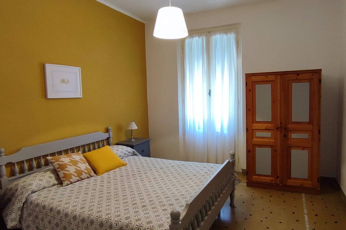 A bedroom with a bed, a nightstand, a lamp, a wardrobe, and a window with curtains.