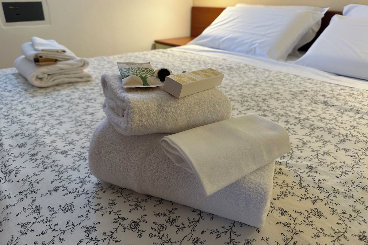 A neatly made bed with a floral-patterned bedspread, a folded towel, and a small box on top.