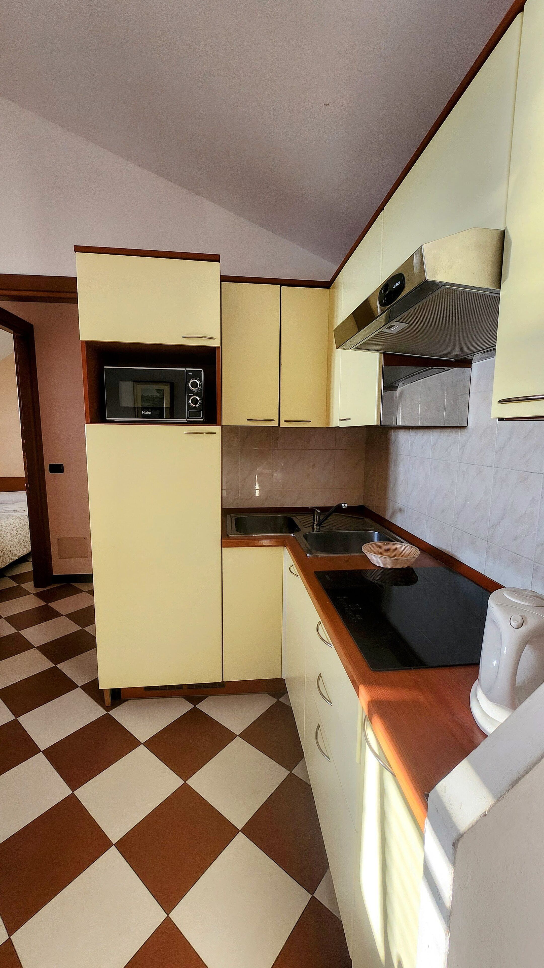 Cocina compacta con microondas, estufa y lavabo. El piso tiene un diseño de cuadros.