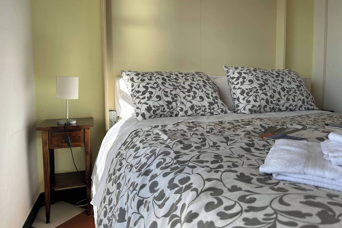 A neatly made bed with patterned bedding, a bedside table with a lamp, and a folded towel on the bed.
