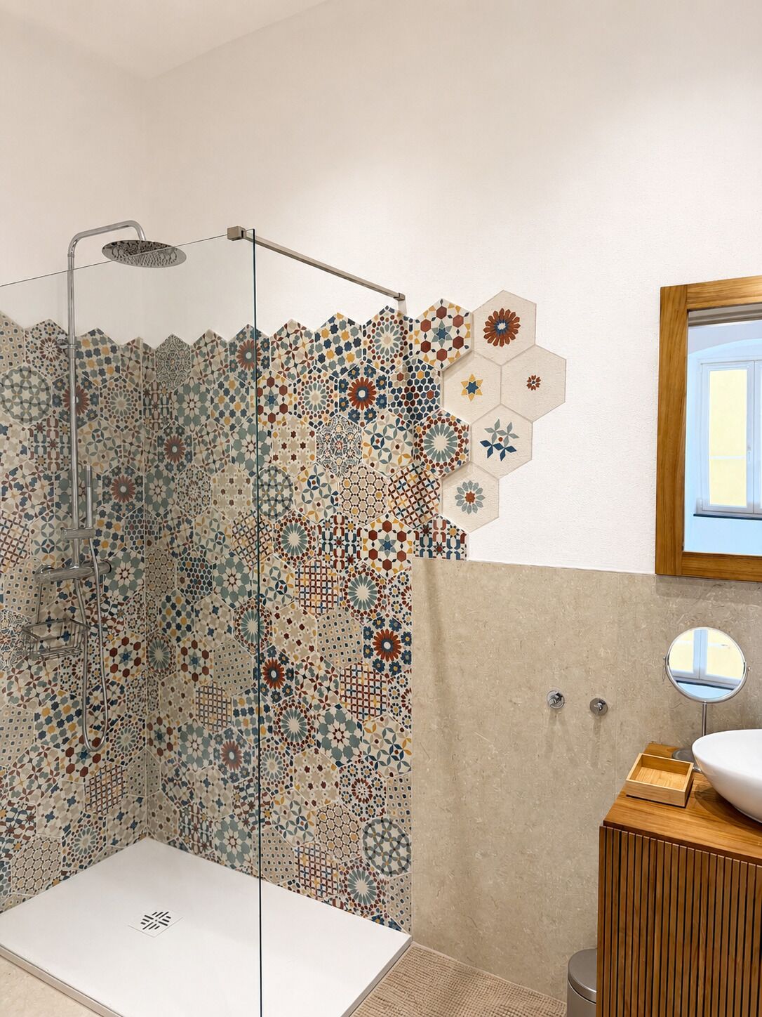 A shower with a glass door, a sink with a wooden cabinet, and a mirror on the wall.